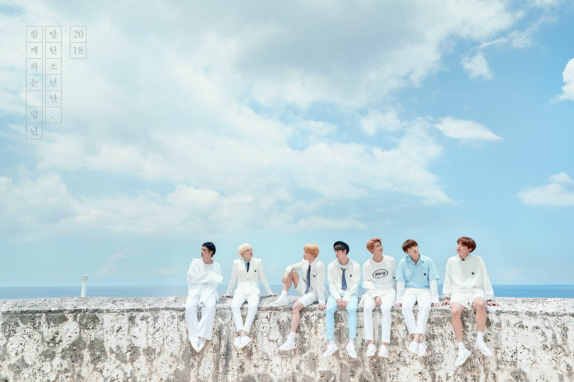 BTS جالسون على حافة حجرية تحت السماء خلفية