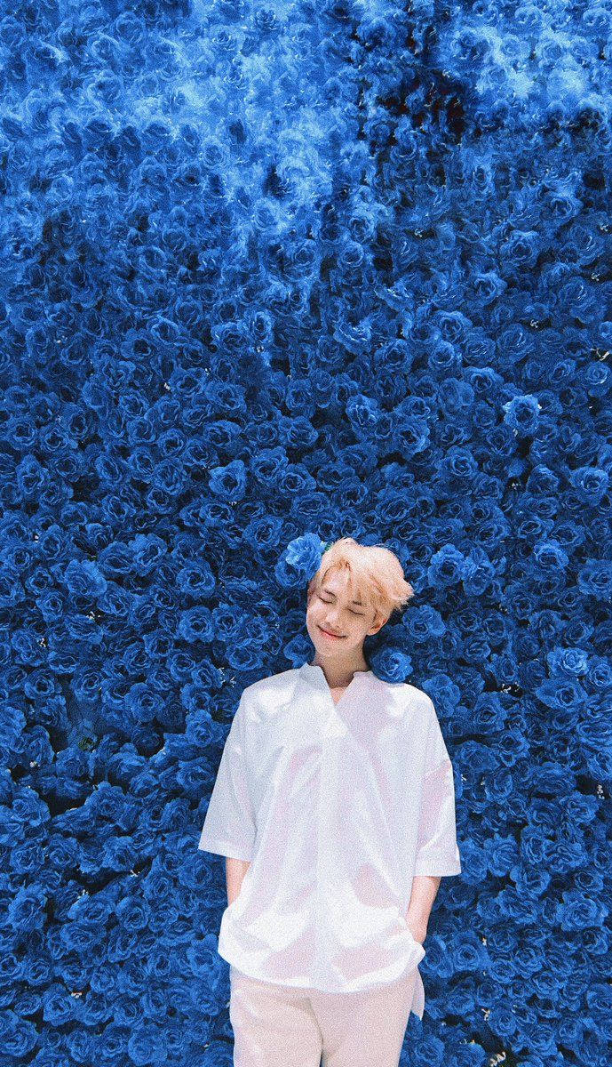 عضو BTS يقف أمام جدار مليء بالزهور الزرقاء.