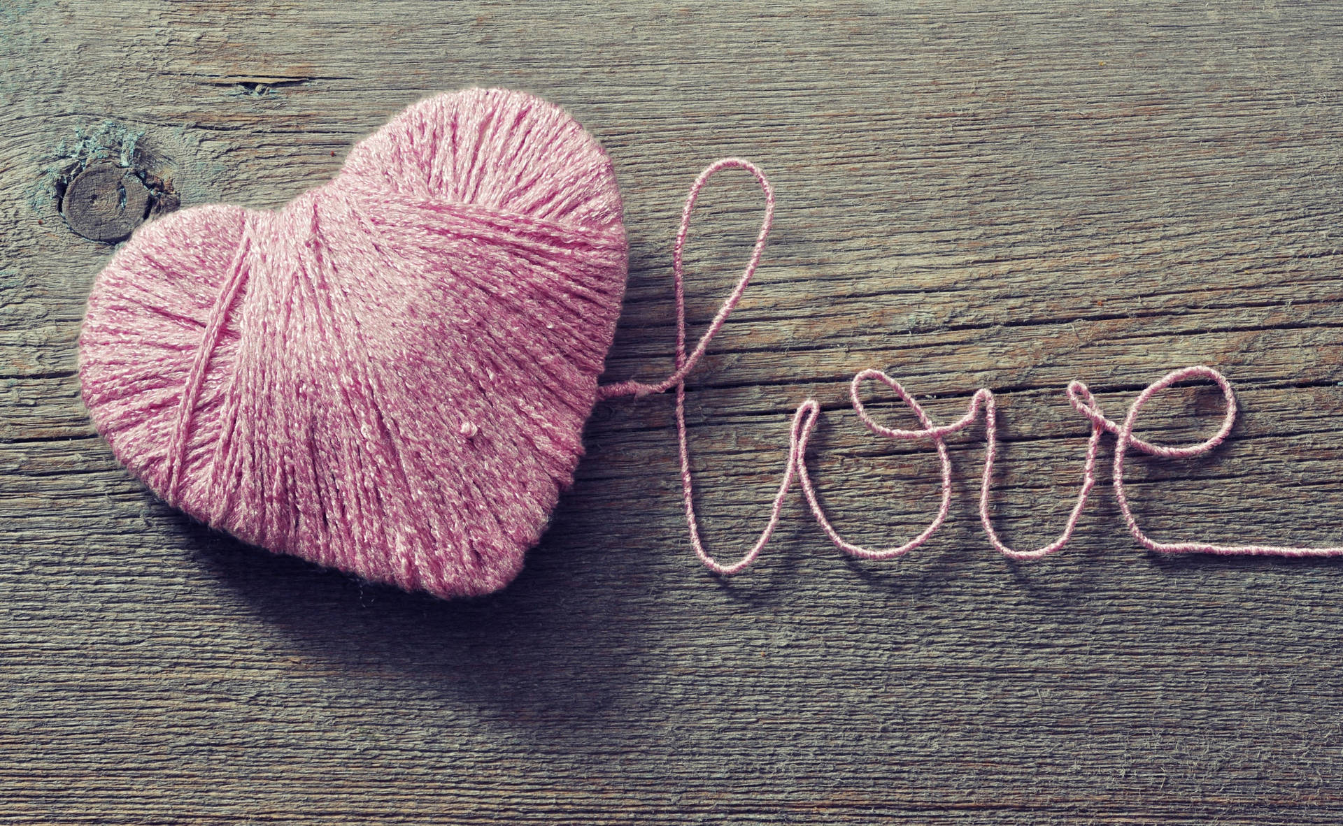 كلمة 'Love' الرومانسية مكتوبة بخيط وردي يشكل قلبًا على طاولة خشبية بمناسبة عيد الحب.