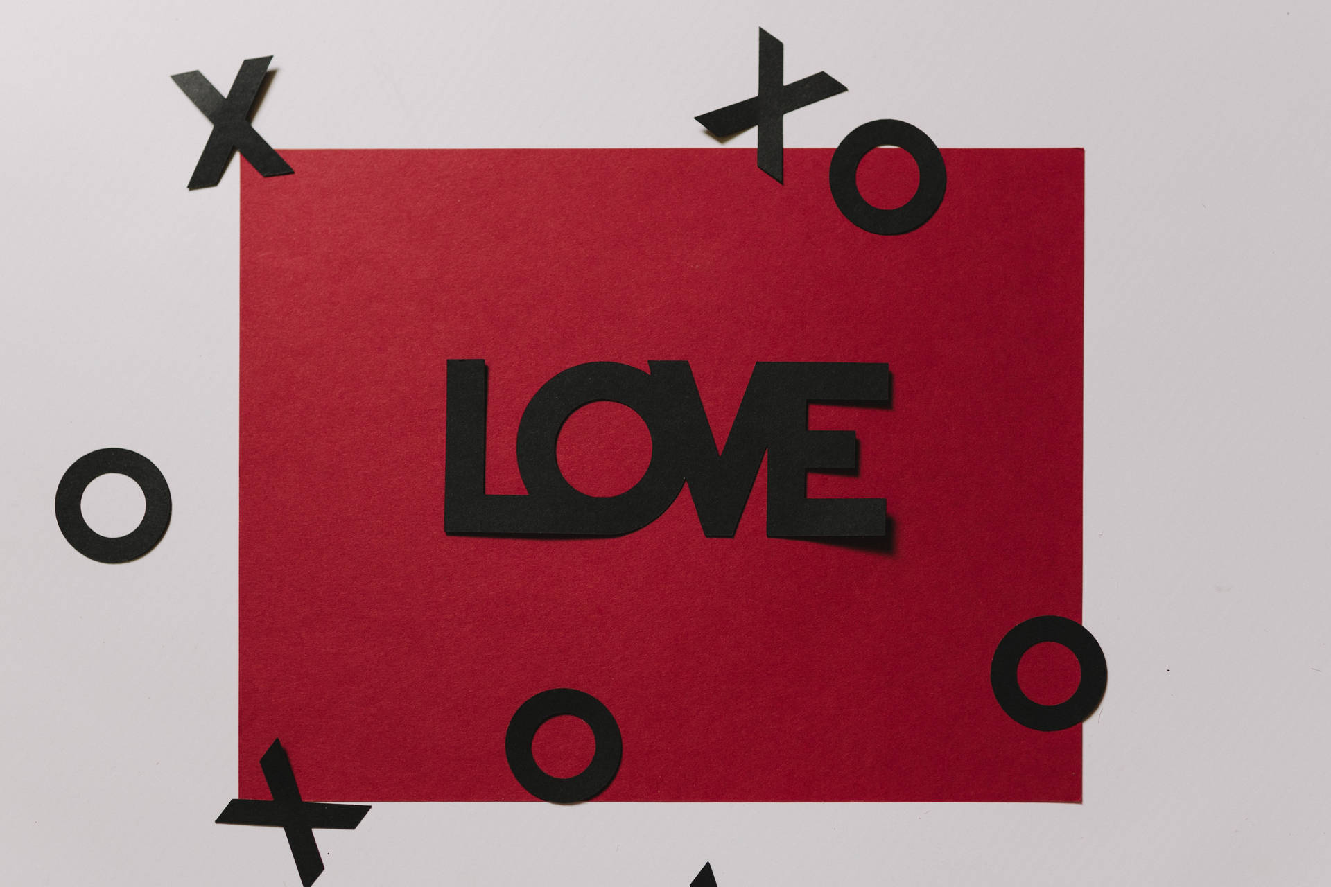 رسالة حب حمراء مكتوب عليها "Love" بالأسود مع قصاصات عائمة من XOXO على سطح أبيض.