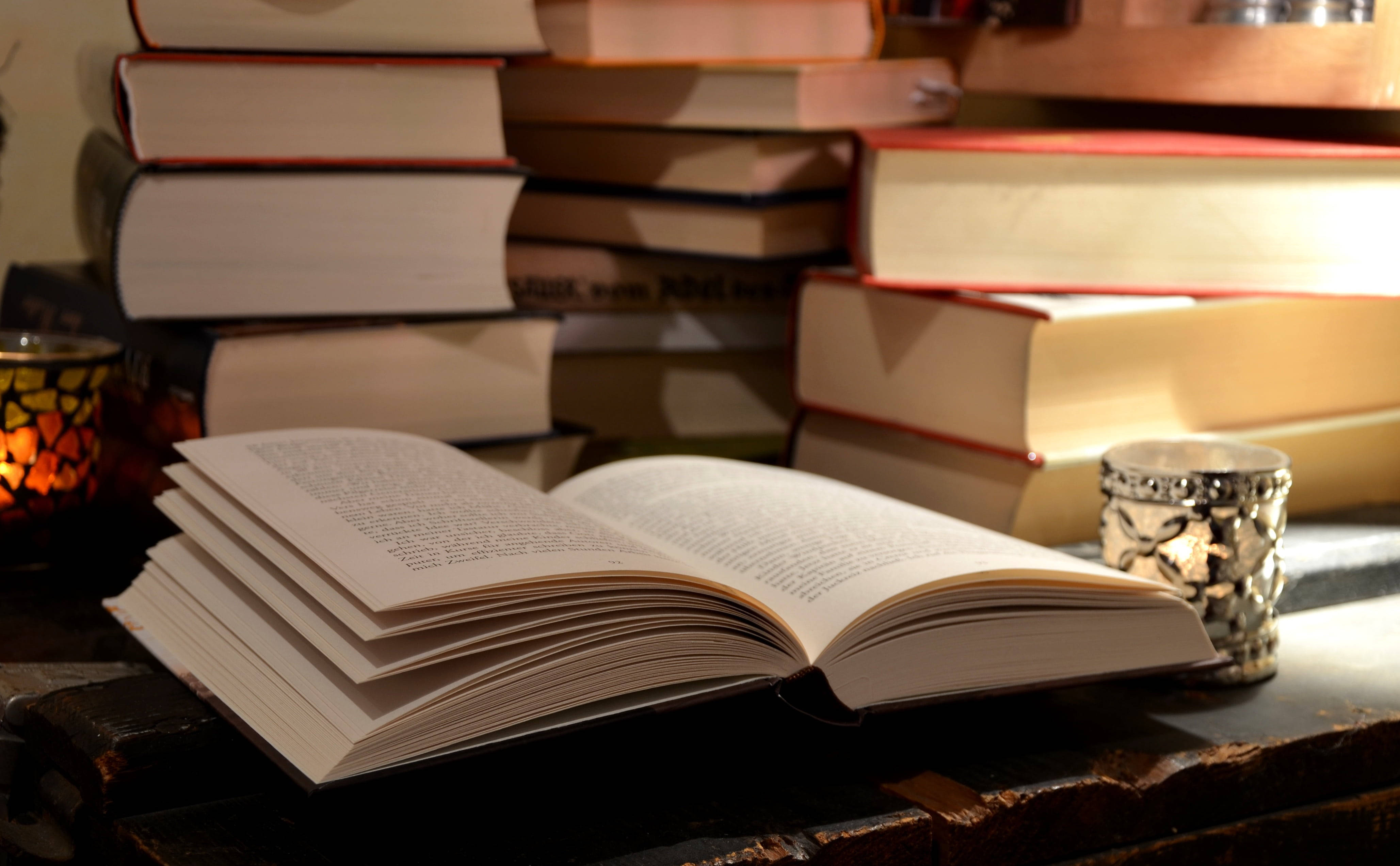 صورة لكتاب مفتوح على مكتب، محاط بمجموعة من الكتب المرجعية الأخرى خلفية