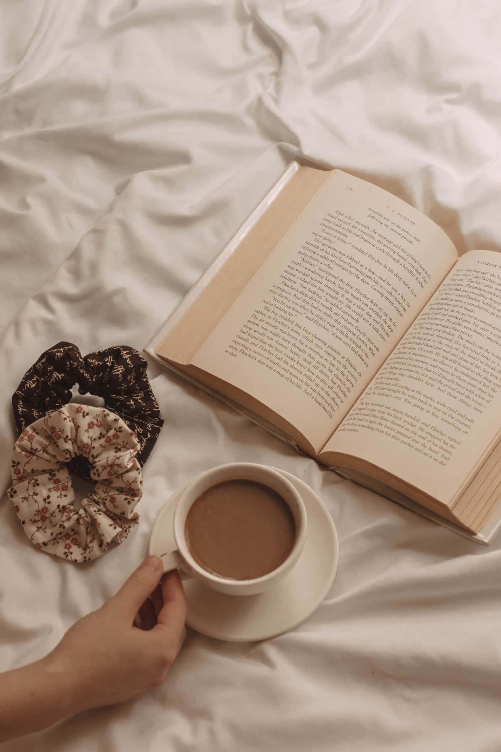 يد امرأة تمسك كتابًا وفنجان قهوة خلفية