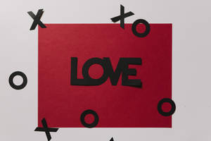 رسالة حب حمراء مكتوب عليها "Love" بالأسود مع قصاصات عائمة من XOXO على سطح أبيض.