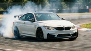 سيارة BMW M4 بيضاء تنزلق حول منعطف على حلبة سباق مع دخان الإطارات وضبابية الحركة. — بي إم دبليو خلفية